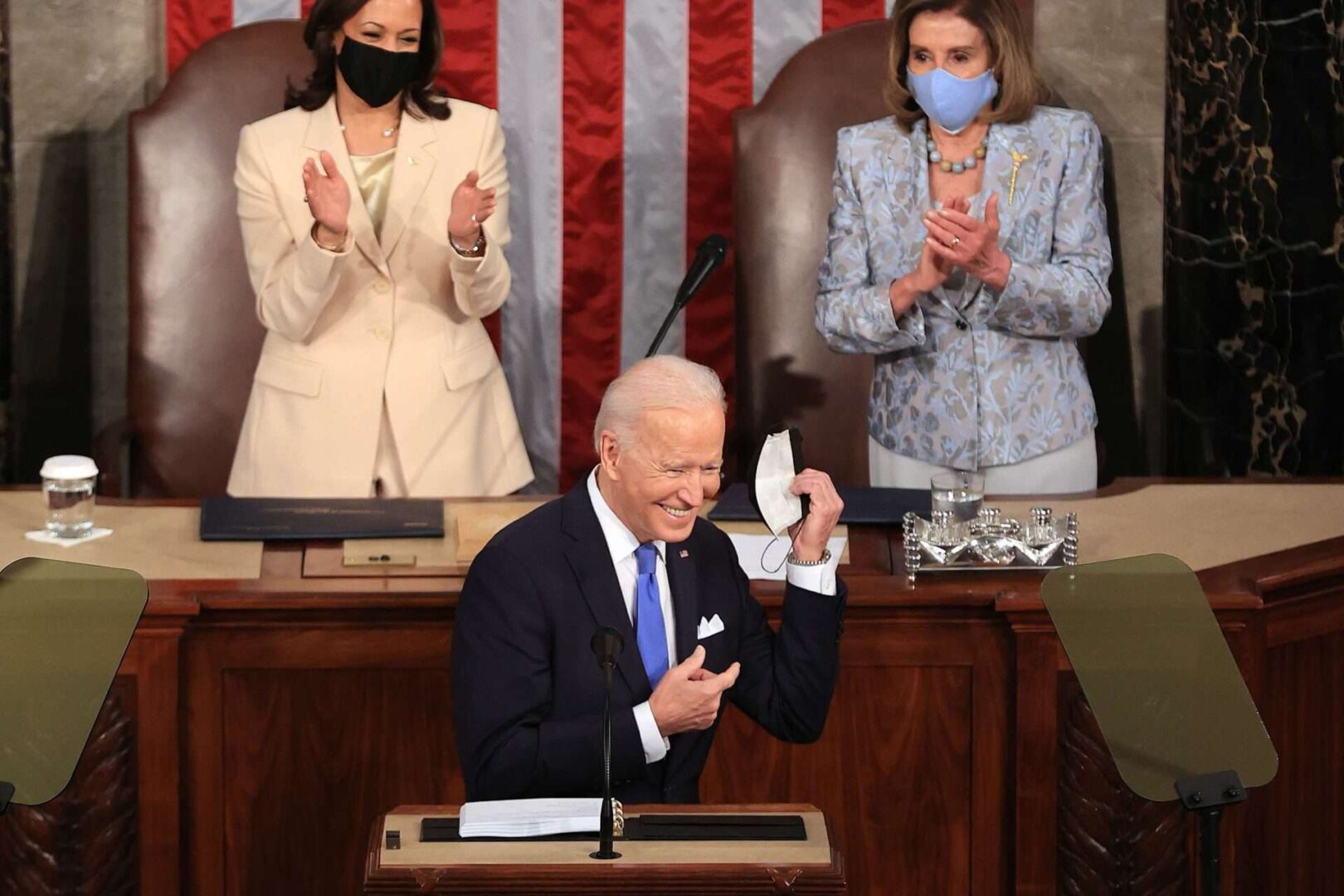 President Joe Biden removes his face mask before addressing a joint session of Congress, as Vice President Kamala Harris and Speaker Nancy Pelosi look on.