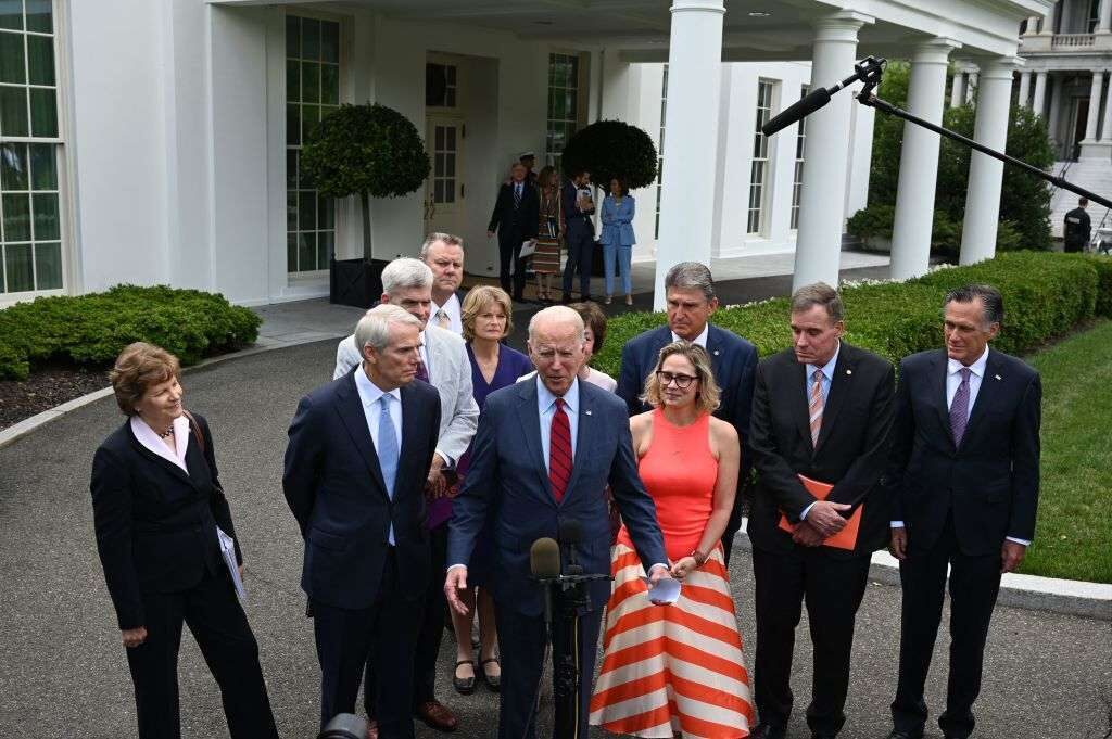 Flanked by five Democratic and Republican senators, President Joe Biden discusses a agreement on infrastructure Thursday outside the West Wing.