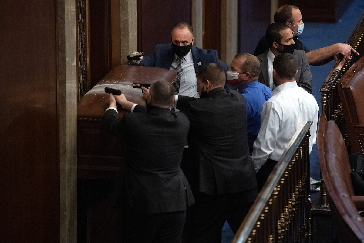 Security barricades the House chamber as rioters disrupt the joint session of Congress to certify the Electoral College vote on Jan. 6, 2021. Reps. Troy Nehls, R-Texas, blue shirt, and Markwayne Mullin, R-Okla., right, are also pictured. President Donald Trump issued pardons to all those involved in the attack.