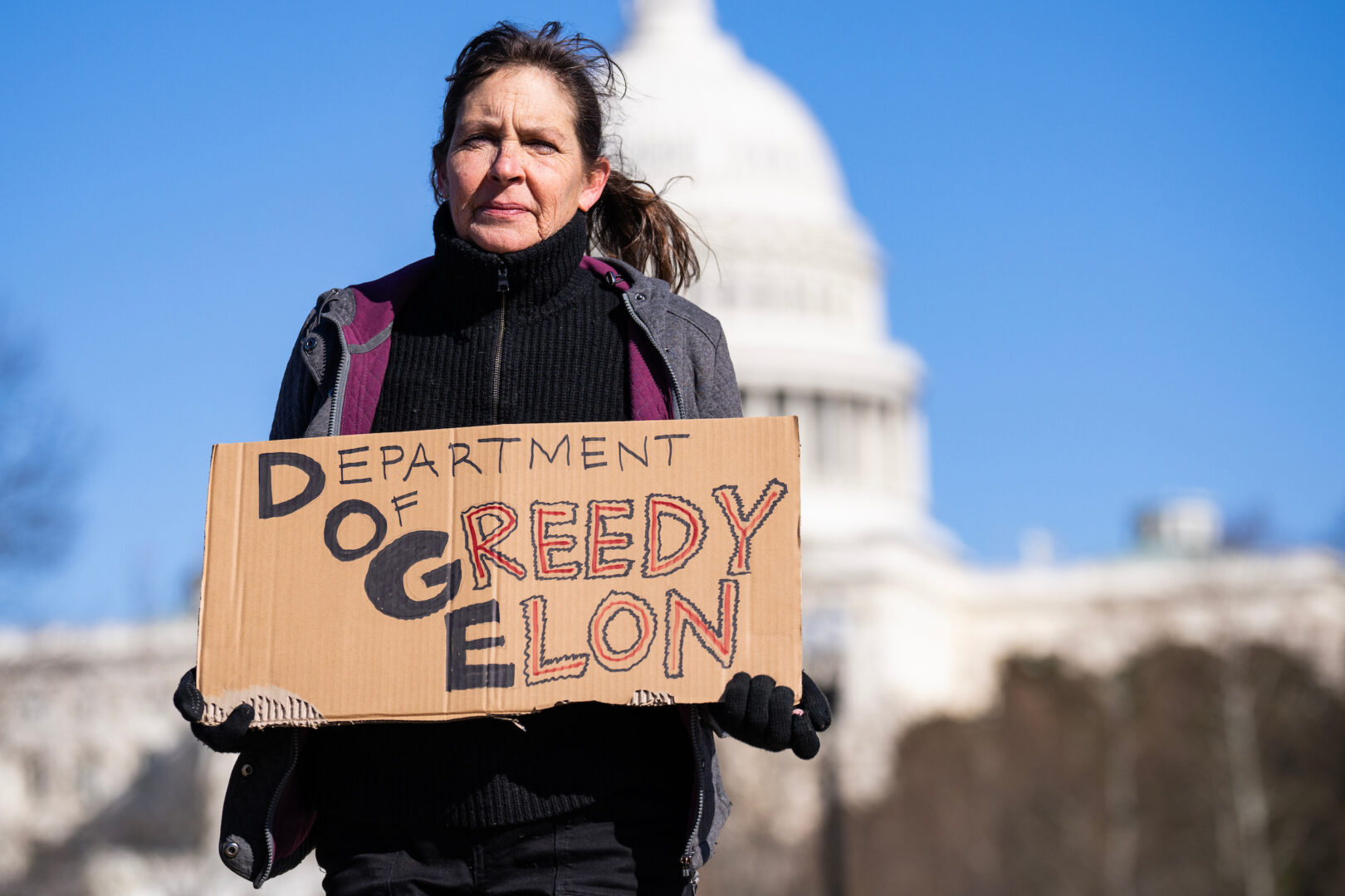 A demonstrator holds a DOGE sign during the "No Kings Day" protest to oppose the Trump administration’s policies including efforts to cut the federal workforce, at the Capitol Reflecting Pool on Monday.