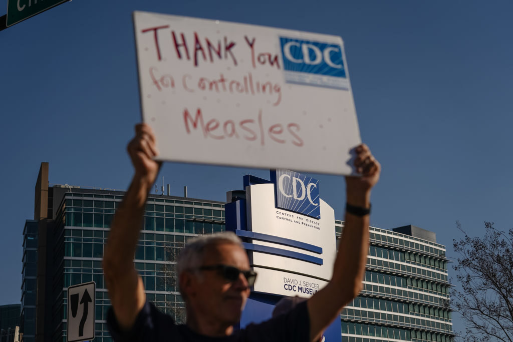 People protesting personnel cuts at the Centers for Disease Control and Prevention hold signs outside the organization's main headquarters on Wednesday in Atlanta. (Elijah Nouvelage/Getty Images)